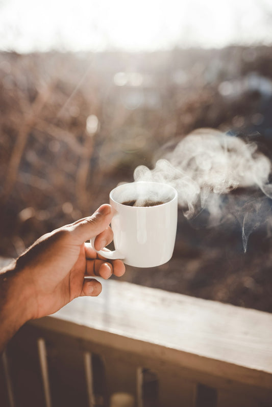 Person holding a white ceramic cup of hot coffee, representing daily coffee drinking and hydration