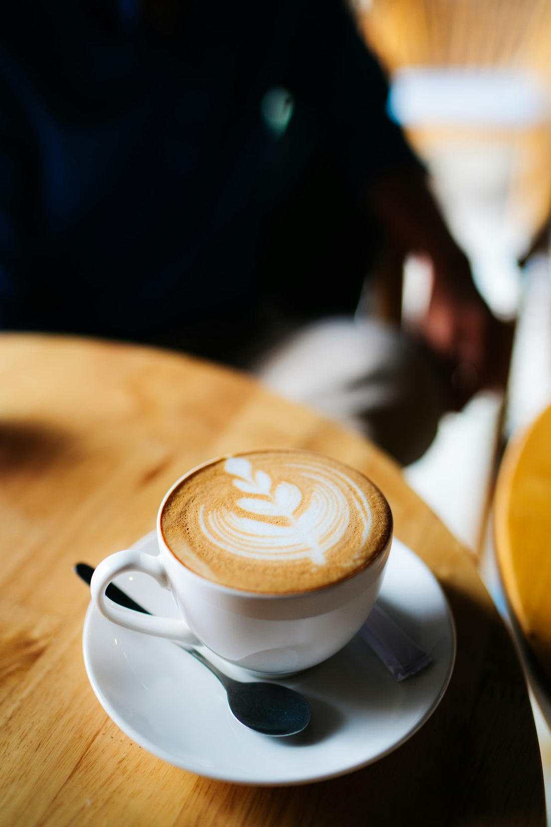 Latte art being poured into a ceramic cup showing a leaf pattern