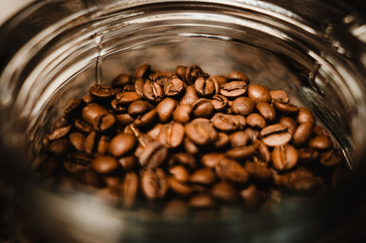 A glass jar filled with freshly roasted coffee beans on a kitchen countertop