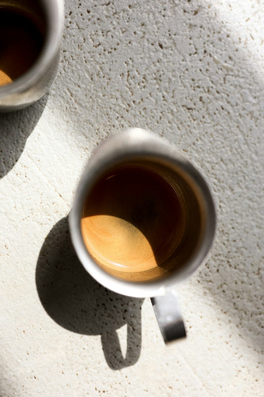 Two metal cups of espresso with rich golden crema on a warm surface